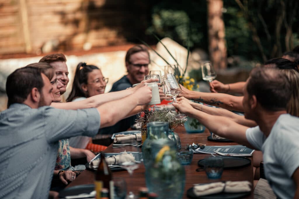 Gruppe stößt mit Getränken an bei Abendessen im Garten in LUKE'S Wohnzimmer