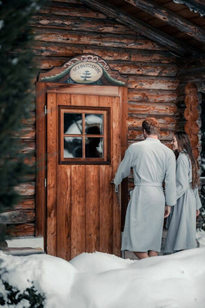 Pärchen im Schnee vor Blocksauna im Sendlhofer's