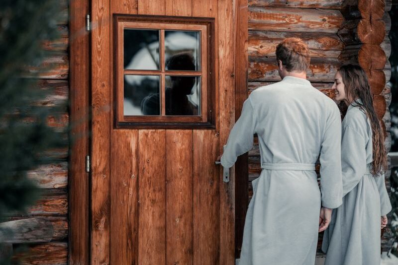 Pärchen im Schnee vor Blocksauna im Sendlhofer's
