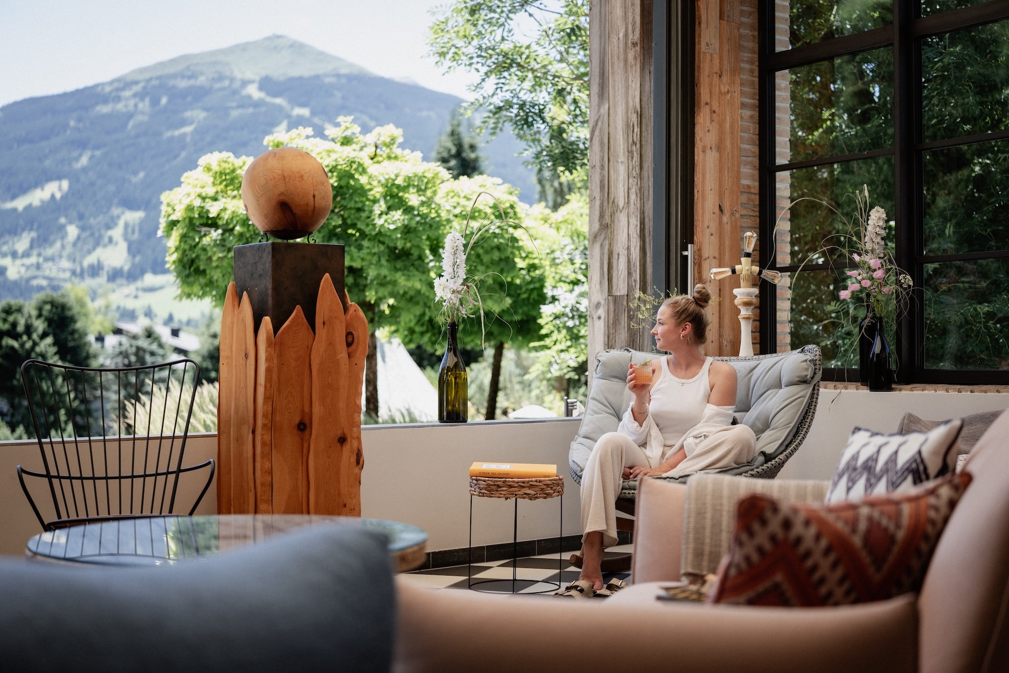 Frau sitzt im Loungechair im Wintergarten mit offenem Bergpanorama