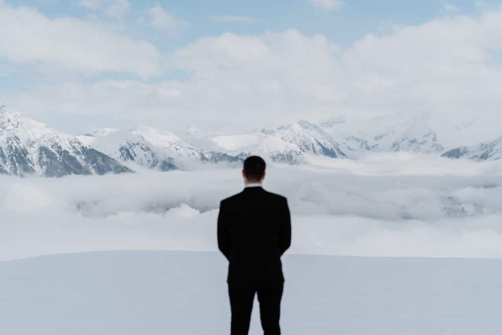 Bräutigam steht auf verschneitem Berggipfel
