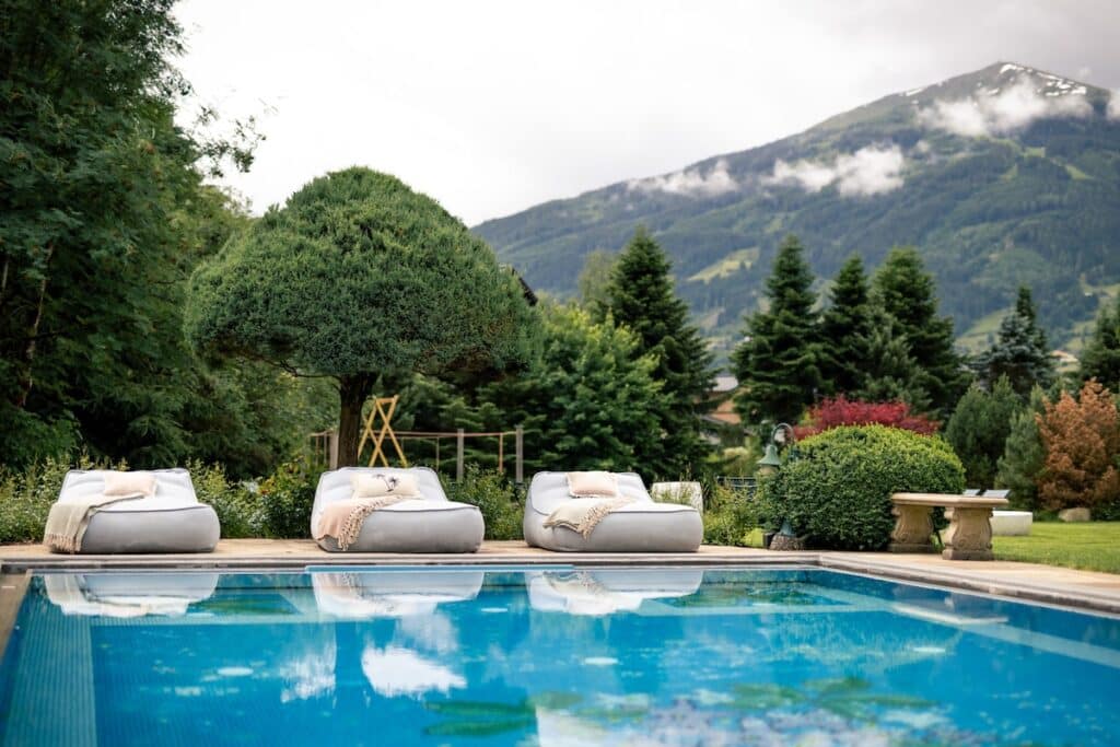 Outdoorpool mit Sonnenliegen im Hintergrund, auch zu sehen der Slacklinepark und die Berge